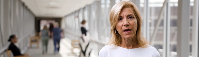 A still of a woman speaking in a hallway — the hallway is an example of a background plate.